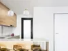 A modern kitchen interior with wooden cabinets, a white countertop, and a black door in the background. Two pendant lights hang from the ceiling. Produktbild-Vorschau