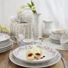A table setting with a floral-patterned porcelain tea set, including cups, a vase, a pitcher, and bowls, with a dessert of dumplings and cream. Produktbild-Vorschau