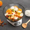A digital kitchen scale with a glass bowl filled with oranges, limes, and sugar, placed on a dark gray surface. Produktbild-Vorschau
