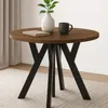 A round wooden table with black metal legs, decorated with a vase of plants and a mug. Podgląd zdjęcia produktu