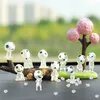 A collection of small, whimsical figures resembling forest spirits, arranged on a surface with a blurred natural background and a decorative pink tree. Produktbild-Vorschau