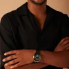 A close-up shot of a person wearing a black shirt and a watch. Produktbild-Vorschau