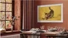 A dining room with a table set for a meal, featuring a Samsung Frame TV displaying a painting of a cat. Produktbild-Vorschau