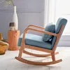 A blue upholstered rocking chair with wooden frame, positioned next to decorative items in a room. Produktbild-Vorschau
