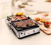 A close-up shot of a grill with steaks and vegetables cooking on it, with some bread rolls and a bowl of tomatoes in the background. Podgląd zdjęcia produktu
