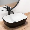 A black and white vessel sink with a black faucet is shown on a wooden floor, with a mirror reflecting the faucet and sink. Náhled obrázku produktu