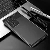 A smartphone case with a carbon fiber texture is placed on a laptop keyboard, with two pens nearby. Voir les images du produit