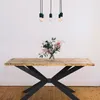 A wooden dining table with a black metal base and a vase of flowers on top, set against a white wall and wooden floor. Produktbild-Vorschau
