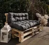 A dark gray pallet sofa with cushions sits on a wooden deck, with a white lantern and dried grass in a vase nearby. Anteprima dell’immagine prodotto