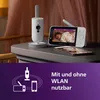A baby monitor set with a camera and a parent unit, placed on a nightstand, with a smartphone and a graphic overlay at the bottom. Produktbild-Vorschau