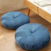 Two round blue floor cushions are placed on a wooden floor next to a modern coffee table with a book on it. Produktbild-Vorschau