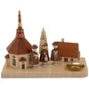 Ein charmantes Holzkunstwerk zeigt ein kleines Dorf mit einer Kirche drei Figuren und einem Baum auf einem Kerzenhalter aus hellem Holz Produktbild-Vorschau
