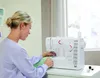 A woman is sewing on a white sewing machine in a well-lit room with a window in the background. Produktbild-Vorschau