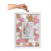 A hand is placing a small wooden heart into a guest book frame with a photo of a bride. Produktbild-Vorschau
