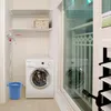 A laundry area with a washing machine, shelves, and a blue bucket. Podgląd zdjęcia produktu
