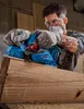 A man is using a blue power planer on a piece of wood in a workshop. Podgląd zdjęcia produktu