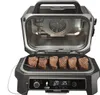 An open electric grill with steaks cooking on the grill grate. The grill has a digital display and controls. Voir les images du produit