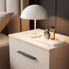 A bedside table with a lamp, books, and perfume bottles. Produktbild-Vorschau
