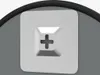 A close-up view of a white square button with a plus sign indentation, set against a gray surface and a black curved edge. Náhled obrázku produktu