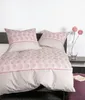 A neatly made bed with pillows and a duvet cover, featuring a pink and beige patterned design. A vase with pink flowers is placed on a shelf to the right. Produktbild-Vorschau