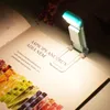 A book is open with a small, clip-on LED reading light attached to the page. The light is illuminating the text. Produktbild-Vorschau