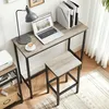 A desk with a laptop, lamp, and coffee, next to a stool, in a home office setting. Produktbild-Vorschau