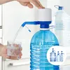 A hand is shown pressing down on a water dispenser pump attached to a large water bottle, dispensing water into a glass. Another large water bottle is visible in the background. Produktbild-Vorschau