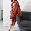 A person wearing a coral-colored hooded blanket sits on a gray sofa. Podgląd zdjęcia produktu