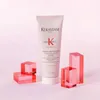 A Kérastase Genesis fondant renforçateur conditioner tube is displayed prominently against a light pink and white background, flanked by decorative red acrylic blocks. Náhled obrázku produktu
