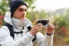 A man in outdoor clothing is holding a smartphone with an accessory attached, appearing to take a photo or video. Anteprima dell’immagine prodotto