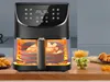 An air fryer with food inside, placed on a wooden surface with other food items in bowls and on a plate. Produktbild-Vorschau