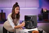 A woman is using a black air fryer in a modern kitchen. The kitchen has purple accent lighting. Produktbild-Vorschau