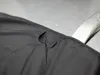 A close-up view of a dark gray fabric mat with a small loop attached to its edge, resting on a wet, light gray surface. Náhled obrázku produktu
