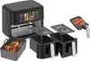 A black dual-chamber air fryer with accessories, including a roasting pan with a chicken and a pizza on a tray. Produktbild-Vorschau