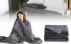 A woman is wrapped in a weighted blanket, and a folded weighted blanket is shown in the lower right corner. A bed with a weighted blanket is in the background. Produktbild-Vorschau