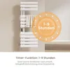 A white electric towel warmer with a towel draped over it, set against a neutral background. A circular graphic overlay highlights a timer function. Produktbild-Vorschau