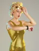 A woman in a gold sequined dress and blonde wig looks at her watch with a surprised expression. Produktbild-Vorschau