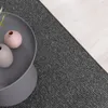 A close-up view of a dark gray carpet next to a light wooden floor, with a gray side table holding two small vases. Produktbild-Vorschau