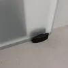 A close-up view of the bottom corner of a frosted glass sliding door, showing a black curved door stop on a concrete floor. Produktbild-Vorschau