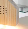 A close-up view of a white and wood-colored electronic device, possibly a speaker or alarm clock, with a wood-grain finish and a series of small holes. Produktbild-Vorschau