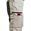 A close-up view of the side pocket of a pair of beige work shorts, showing a small red and black object and a pen inserted into the pocket. Produktbild-Vorschau