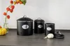 Three black kitchen storage canisters are arranged on a countertop with a decorative branch and a pumpkin in the background. Produktbild-Vorschau