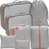 A collection of grey packing cubes and bags with orange zippers and accents, arranged on a white background. Voir les images du produit