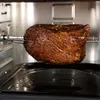 A roast is cooking on a rotisserie spit inside an oven. Produktbild-Vorschau