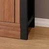 Close-up of the bottom corner of a wooden cabinet with a black metal frame, resting on a wooden floor. Produktbild-Vorschau
