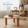 A sewing room with a round wooden table in the foreground, a sewing machine on a desk in the background, and a mannequin with a jacket. Náhled obrázku produktu
