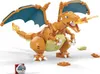 A toy model of Charizard, a Pokemon, is displayed on a white background. The Charizard is orange with blue wings and is breathing fire. Other small toy pieces and a Pokeball are also scattered around. Voir les images du produit