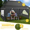 A family is sitting at a table under a gray pop-up gazebo in a grassy yard. Produktbild-Vorschau