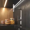 A modern kitchen counter with a faucet, jars of food, and wooden bowls, illuminated by under-cabinet lighting. Produktbild-Vorschau