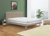 A bedroom scene with a mattress on a bed frame, a small side table, and a plant in the background. Produktbild-Vorschau